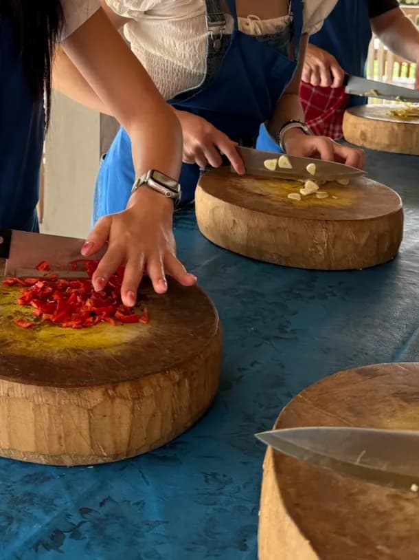 Guests dicing red chili and slicing garlic on round wooden chopping blocks at the Petulu class table