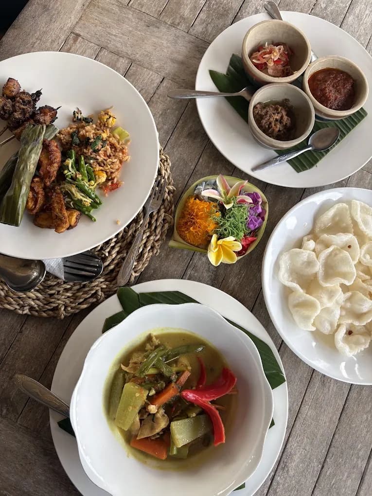 A Petulu class table with sate, banana-leaf pepes, sambal bowls, canang sari, krupuk, and coconut curry, from the Petulu class where ayam betutu is cooked