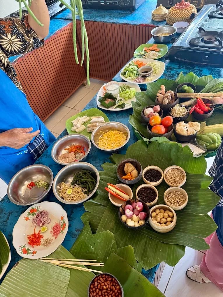 The Petulu class ingredient table: spice roots and seeds on banana leaf, with tofu, corn, long beans, and prepped vegetables