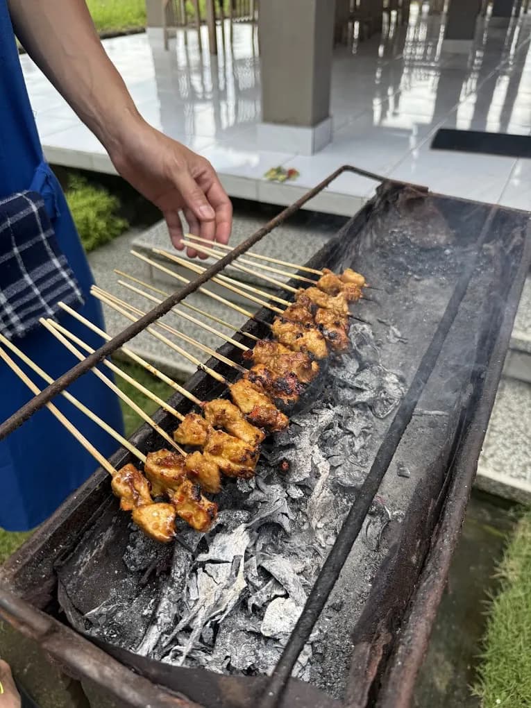 Satay skewers grilling over charcoal beside the Petulu kitchen, from the Petulu class where peanut sauce for sate is cooked