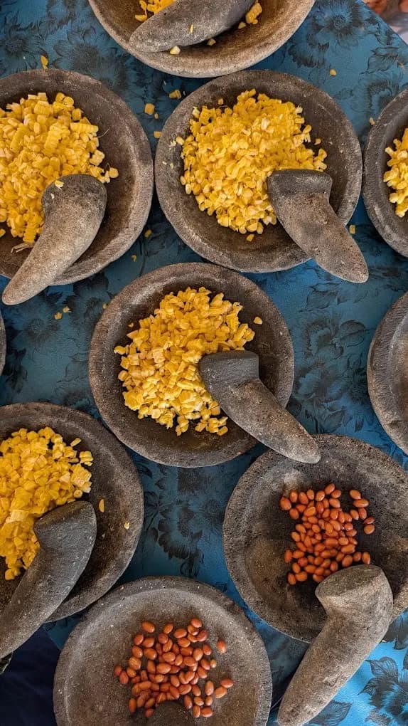 Stone mortars set out with diced corn and peanuts on the blue class table in Petulu
